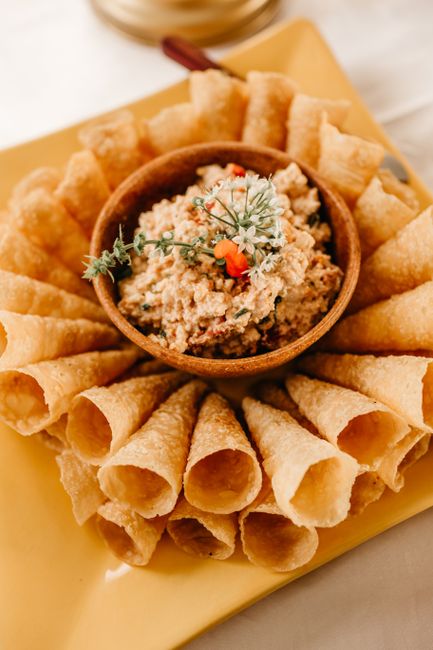 A white bowl of creamy charred corn dip topped with crumbled cotija cheese, chopped cilantro, and a dusting of chili powder, surrounded by tortilla chips for dipping.