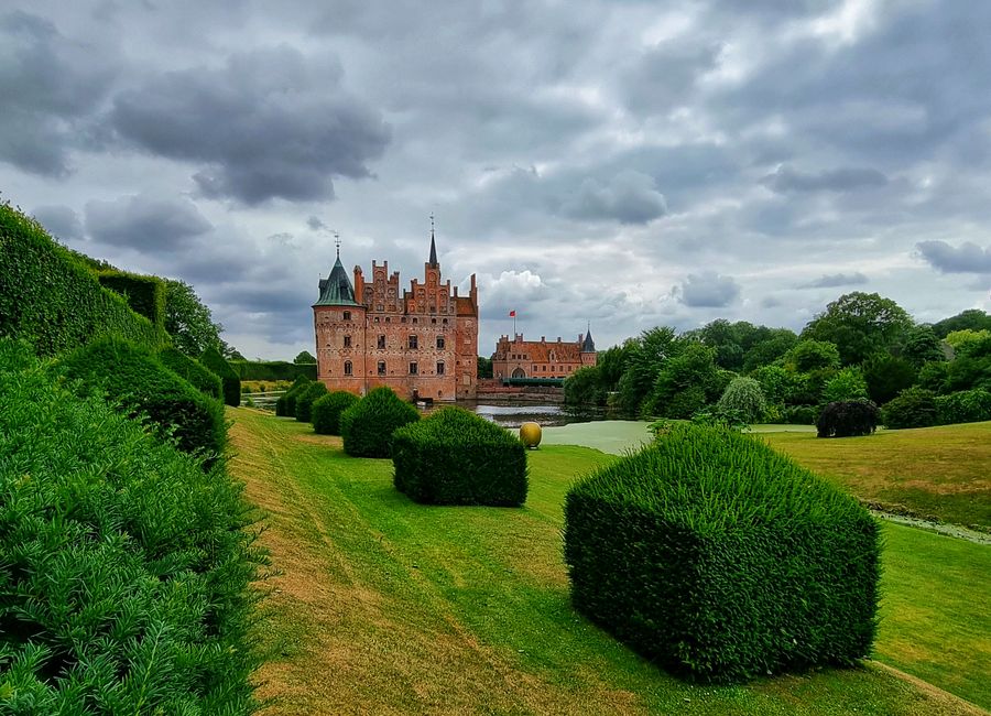 Egeskov Castle surrounded by lush gardens under a dramatic cloudscape in Denmark.
