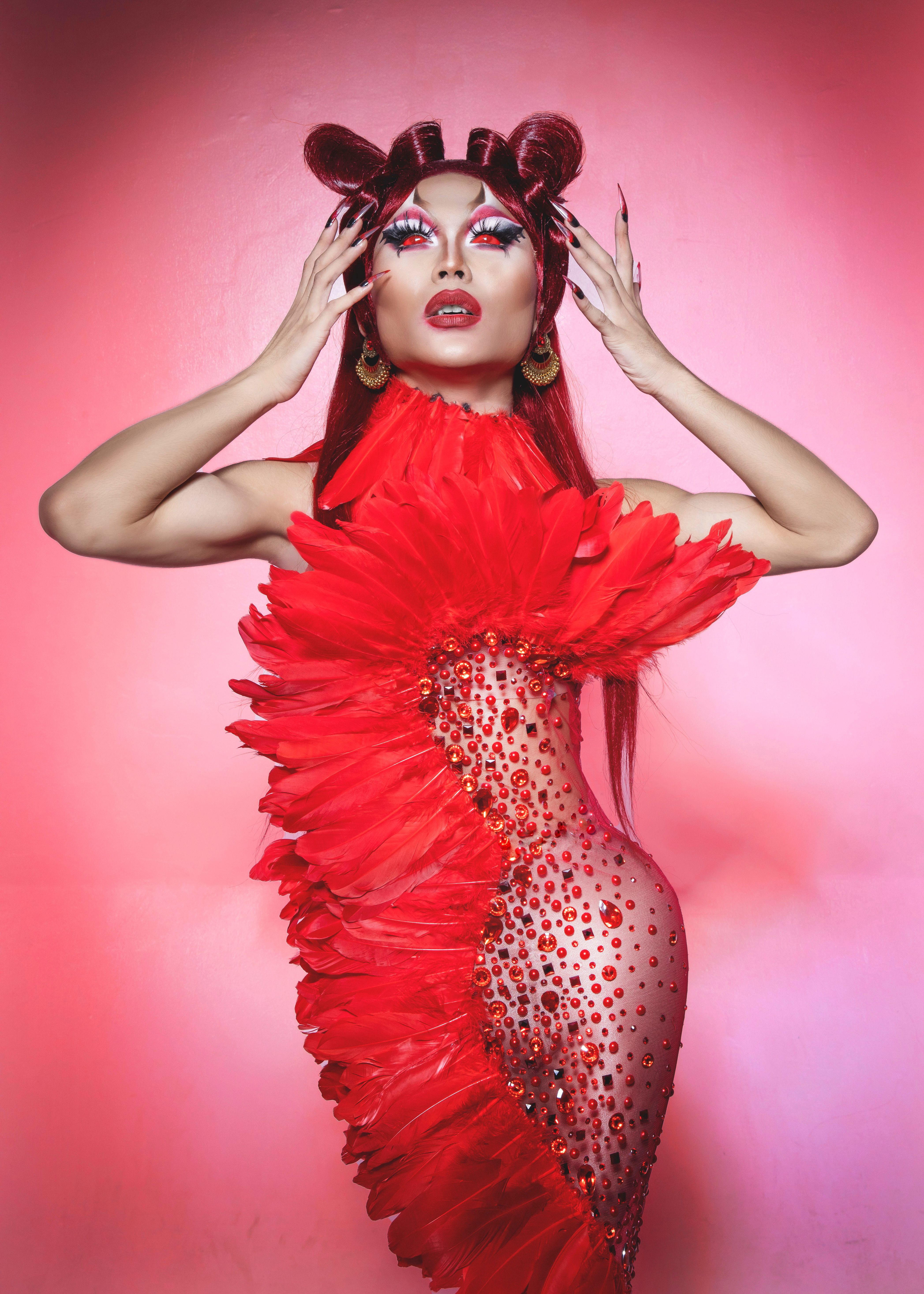 Striking fashion portrait of a woman in an extravagant red dress against a pink background.