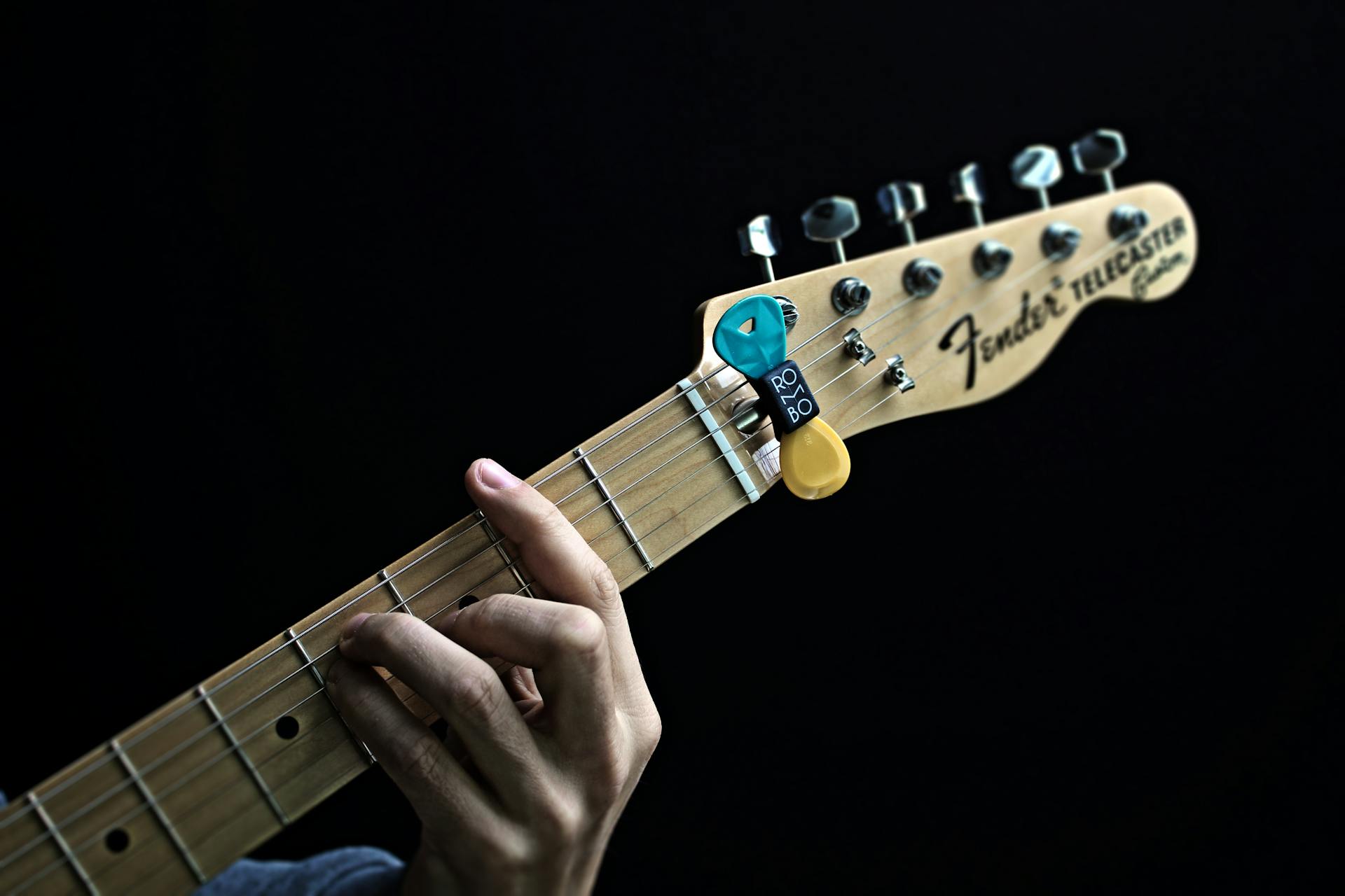 Hand playing a Fender electric guitar with picks attached. High contrast, studio shot.