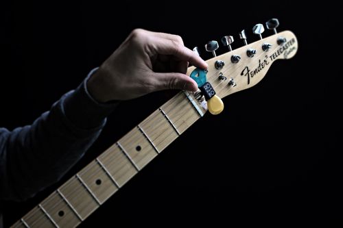 Free Detailed close-up of a hand holding a guitar pick on a Fender Telecaster headstock against a black background. Stock Photo