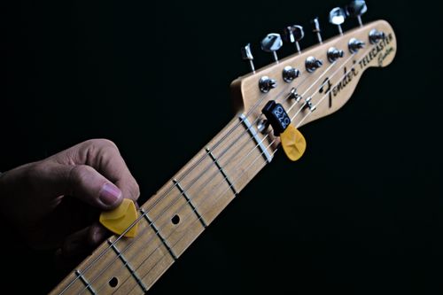 Free Detailed shot of guitar neck with a yellow pick against a black background, ideal for music themes. Stock Photo