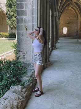 Young woman in a white tank top and sunglasses enjoying a sunny day in a historic cloister garden.