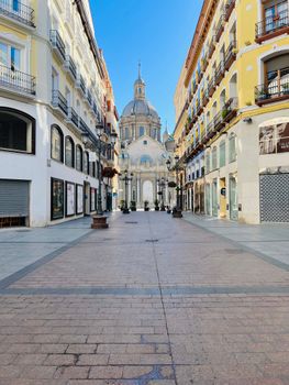 A picturesque empty street in Zaragoza leading to a historic basilica, under clear skies.