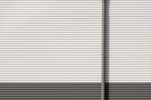 Free Minimalist corrugated metal wall with vertical pipe, showcasing industrial architecture. Stock Photo