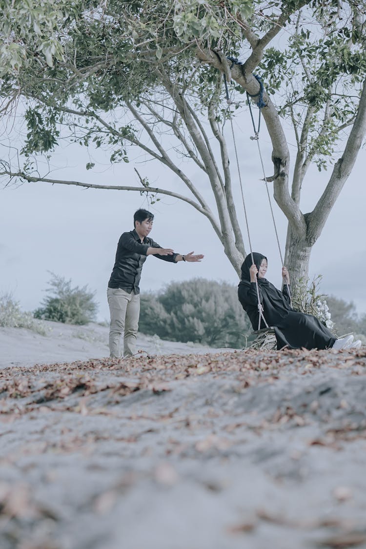 A Man Pushing A Woman Sitting On The Swing 