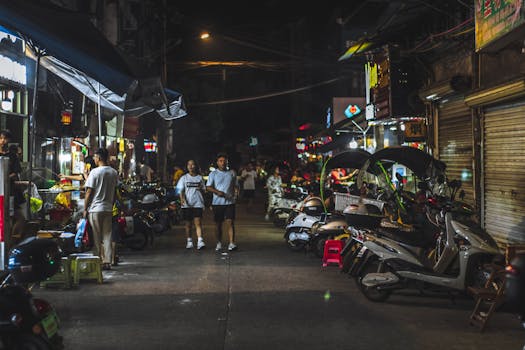 A bustling night market scene with people, scooters, and illuminated shops.