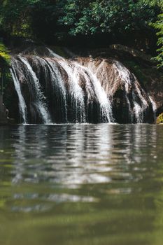 A tranquil waterfall flowing over rocks into a reflective pool surrounded by lush greenery.