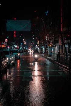 Atmospheric nighttime street scene in Istanbul with cars, motorbike, and wet roads reflecting city lights.
