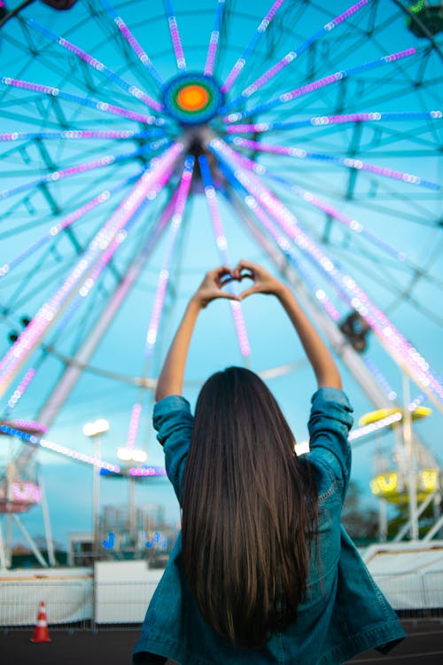 Femme Face à La Grande Roue Tout En Faisant Signe De La Main Du Coeur