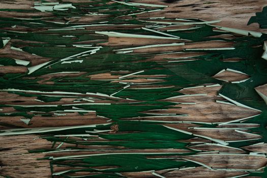 Close-up of weathered green paint peeling on a wooden surface, revealing intricate textures.