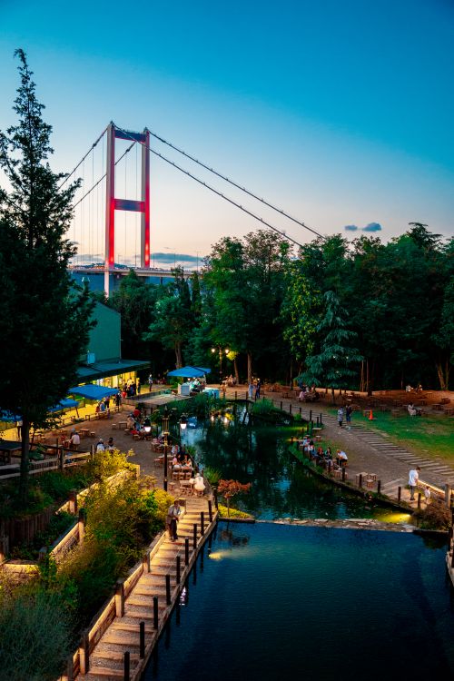 Free Vibrant evening view of the 15 July Martyrs Bridge in Istanbul with a lively park setting and water reflections. Stock Photo