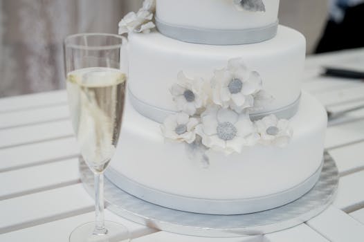 Beautiful three-tier white wedding cake adorned with flowers next to a champagne glass.
