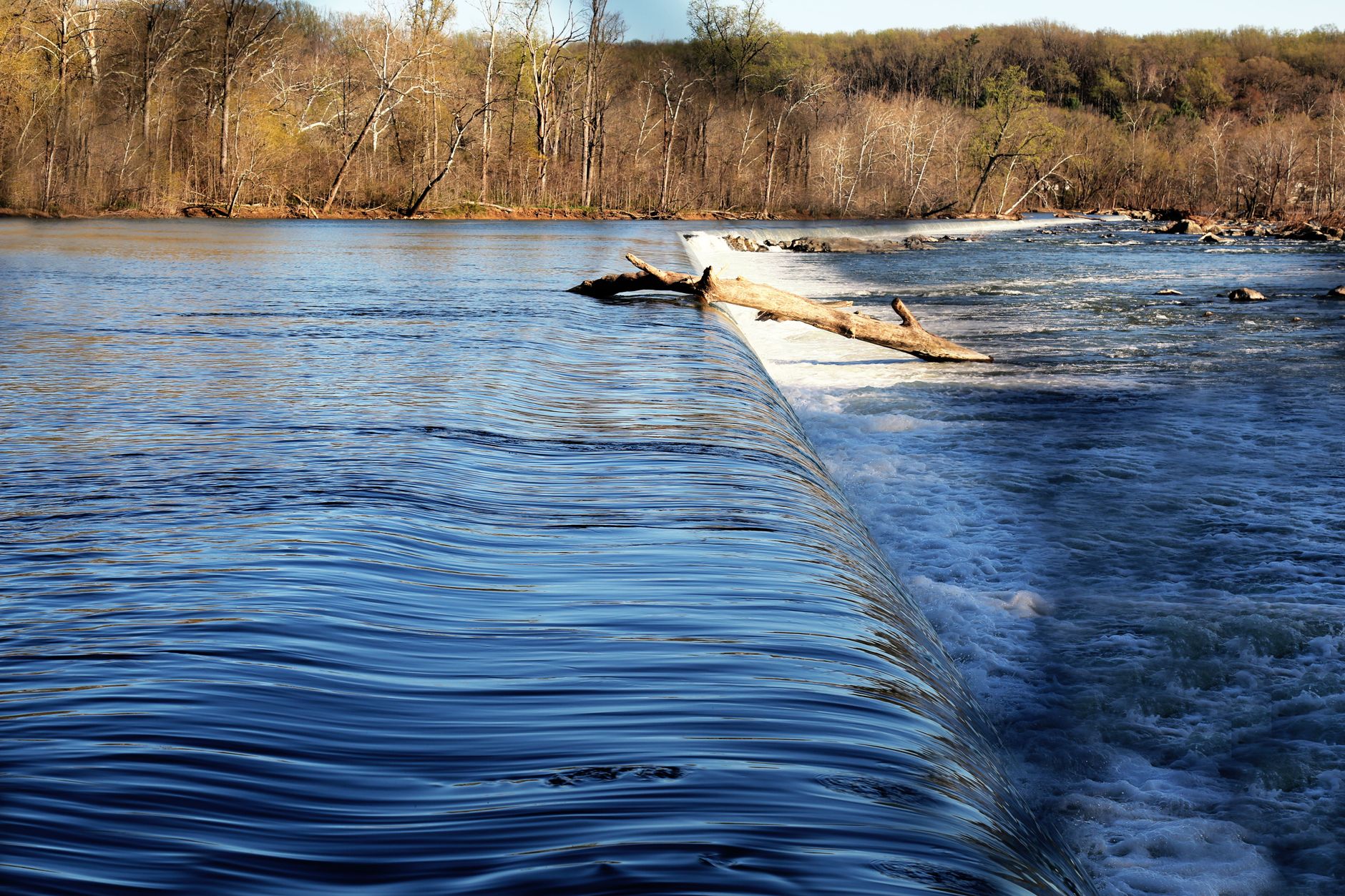 Calm and cascading waters over rocks and tree log at Great Falls, Virginia.