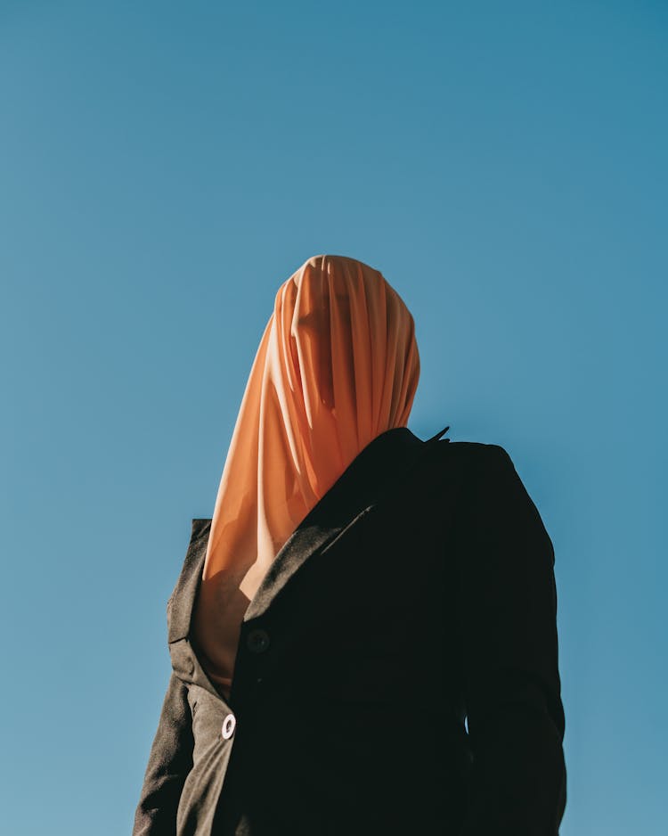 Person Covering Head With Orange Cloth Wearing A Black Blazer