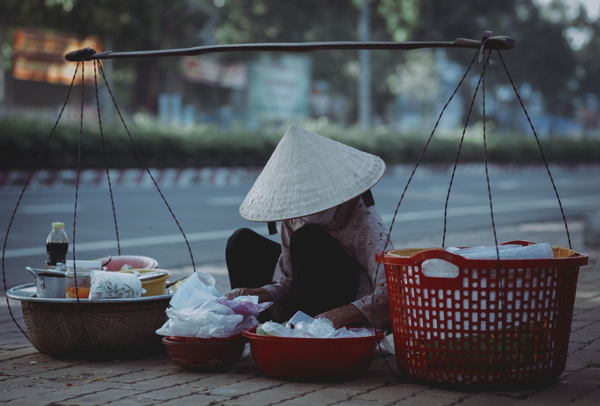 Street vendor in conical hat selling products with baskets on a sidewalk.