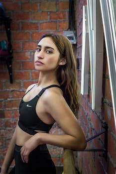 A woman in athletic wear confidently poses against a brick wall indoors.