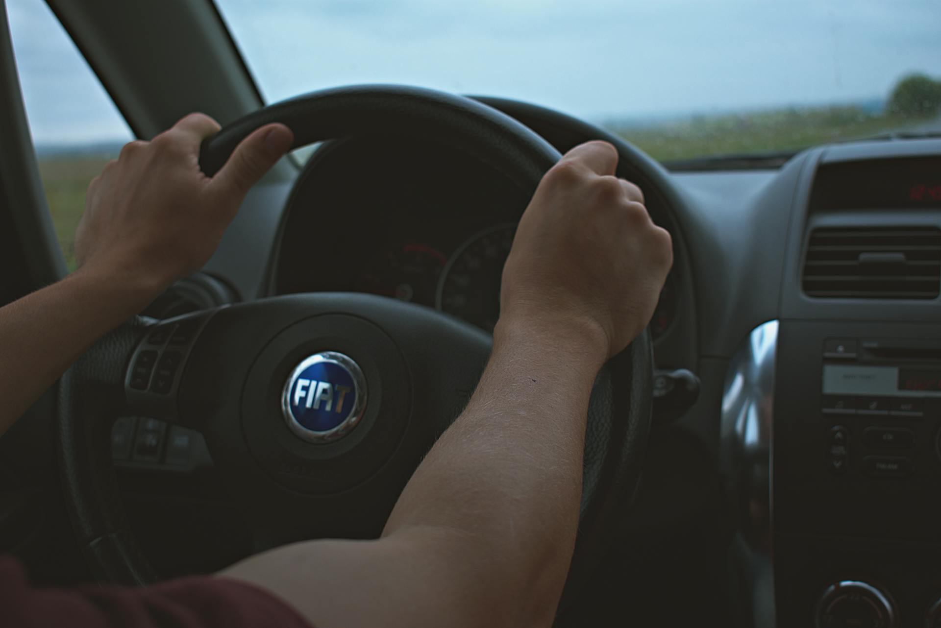 Close-up of hands on the steering wheel of a Fiat car interior, perfect for travel and automotive themes.