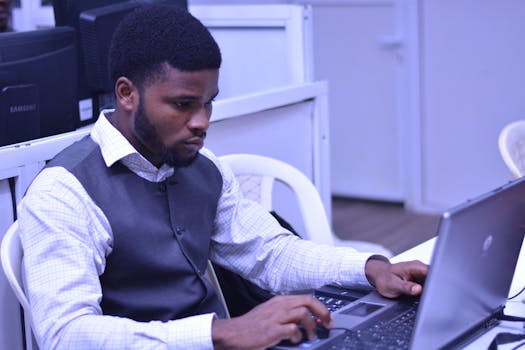 在现代办公环境中，一个留着胡子的年轻人在笔记本电脑前紧张地工作