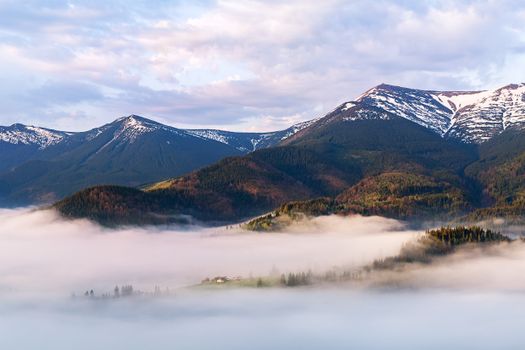 Captivating view of snow-covered mountains rising over a mist-filled valley under a blue sky.