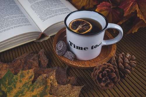 Hot Drink with Lemon Slice on a Mug Beside a Book Near Dried Leaves