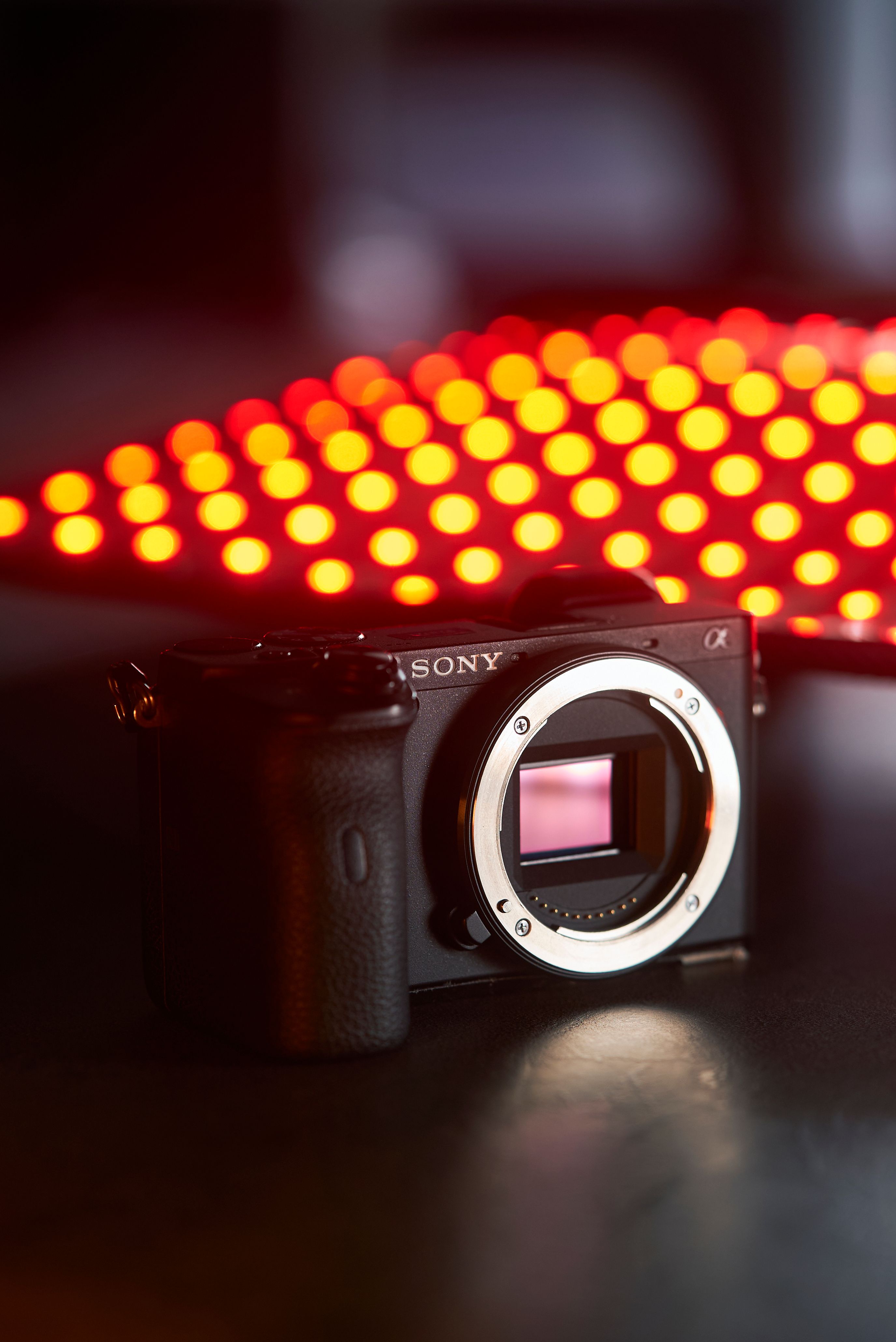 Close-up of a black mirrorless camera body with vibrant red bokeh background.