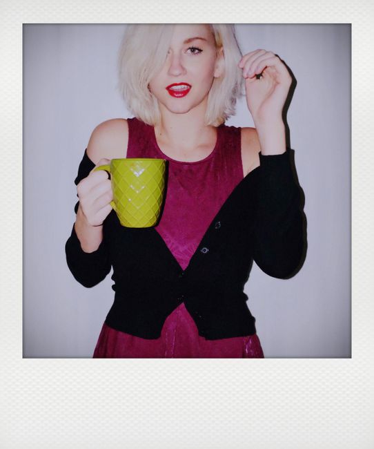 Blonde woman posing indoors with vibrant fashion and coffee mug in a Polaroid-style portrait.