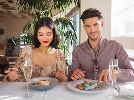 Stylish couple enjoying a gourmet meal with champagne at a sophisticated restaurant setting.
