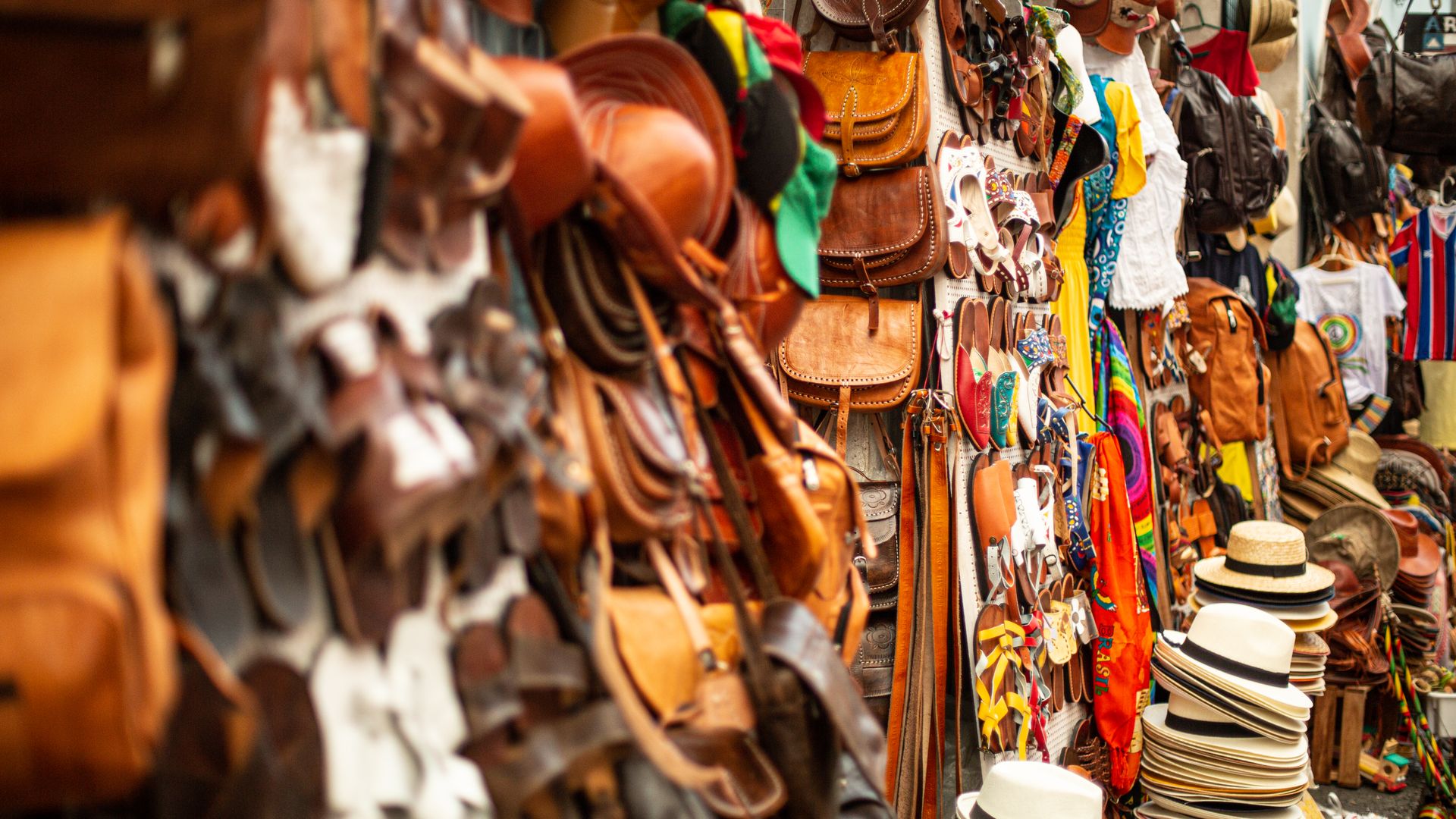 A vibrant assortment of leather goods, hats, and clothing displayed at an outdoor market stall.