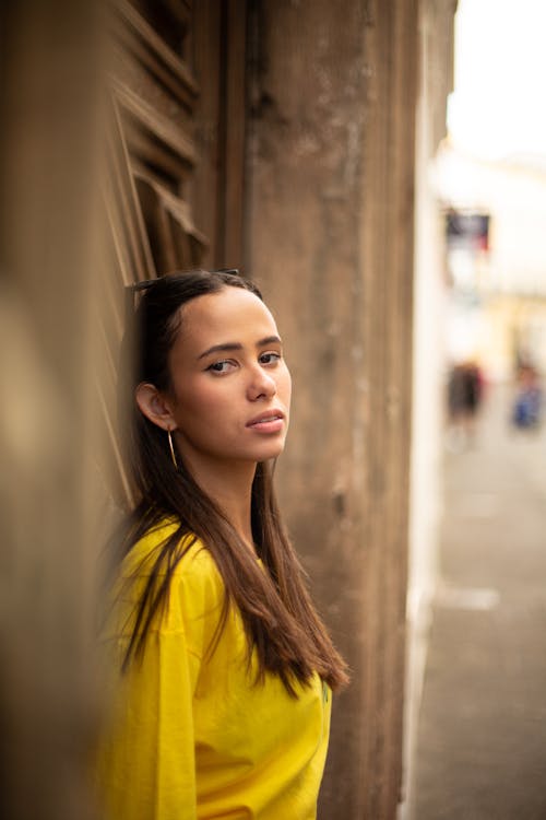 A Woman in Yellow Long Sleeves Leaning on the Wall at the Street