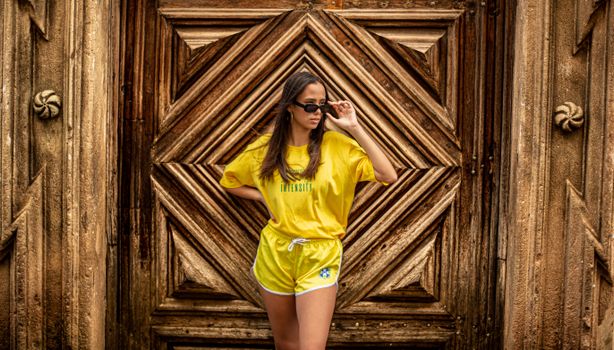 Confident woman posing in bright yellow sportswear in front of a wooden ornate door.