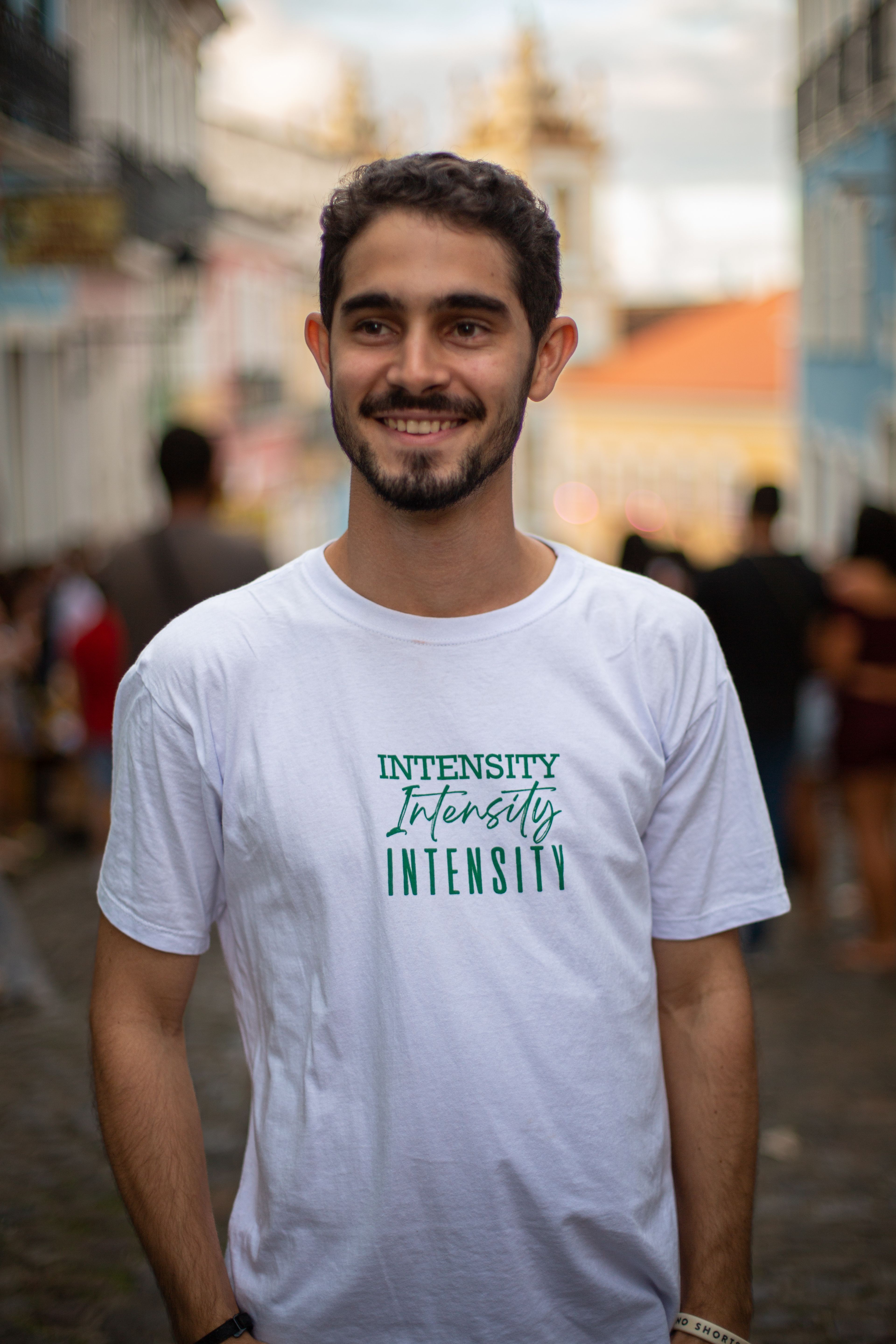Portrait of a smiling man in Salvador, Brazil, wearing a white t-shirt with 'Intensity' text.