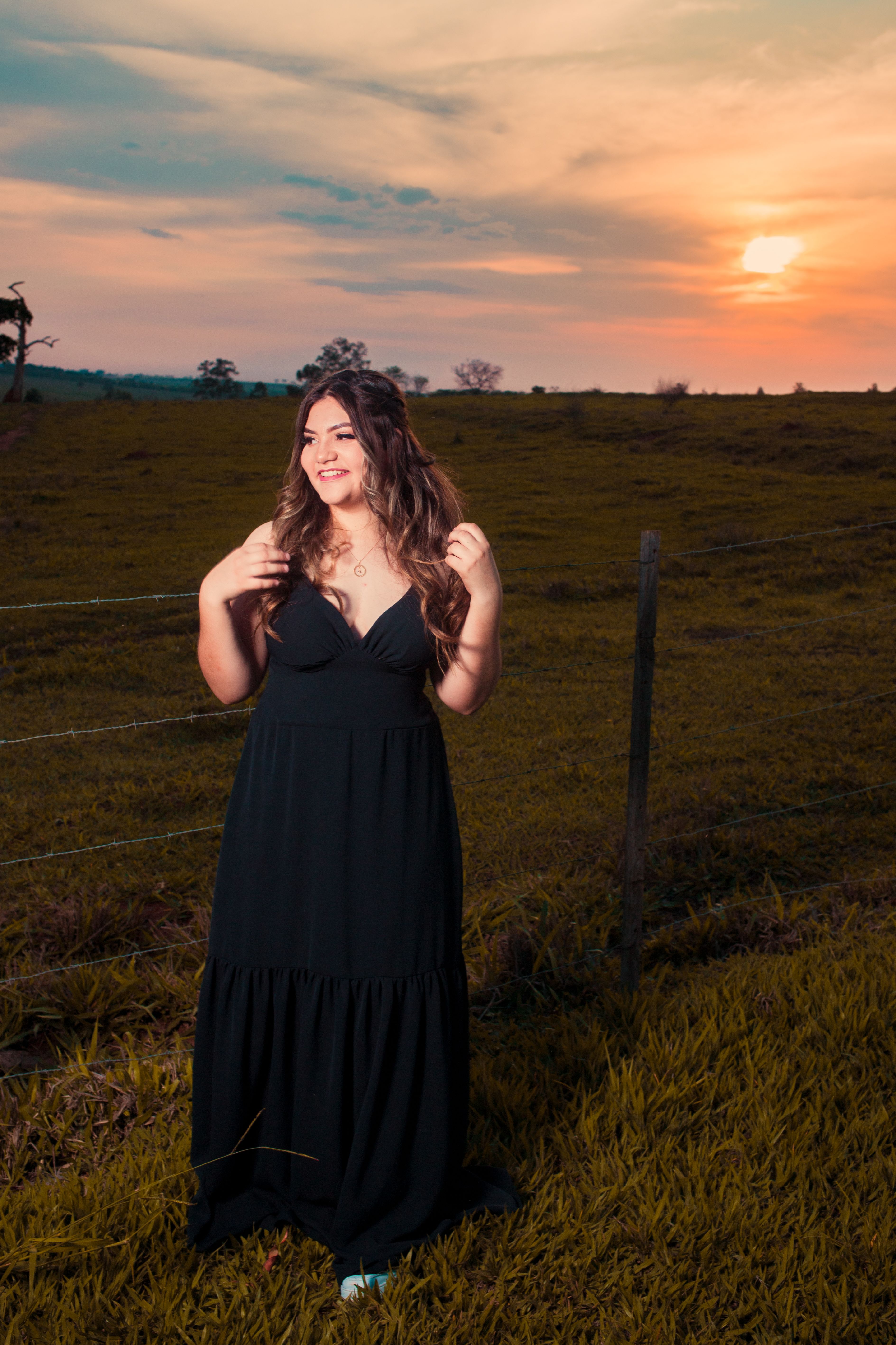 A woman smiles in a rural field at sunset, embodying warmth and serenity.