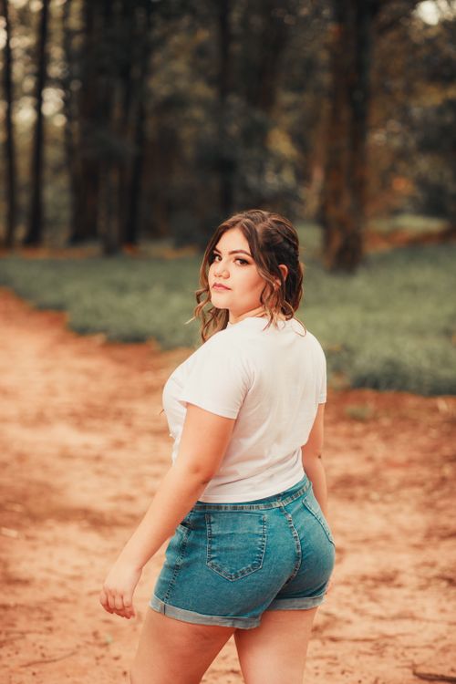 Free Young woman in denim shorts and white shirt walking through a forest pathway. Stock Photo