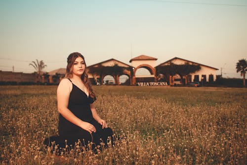 Woman Wearing a Black Dress Kneeling on a Grass Field