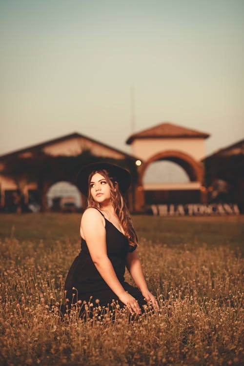 Woman in Black Spaghetti Strap Dress Sitting on Grass Field