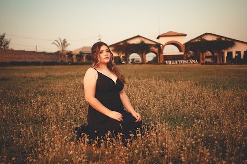 A Woman in a Black Dress Sitting on a Grass Field