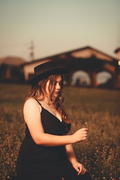 A Woman in a Black Dress Sitting and Holding a Flower on a Grass Field