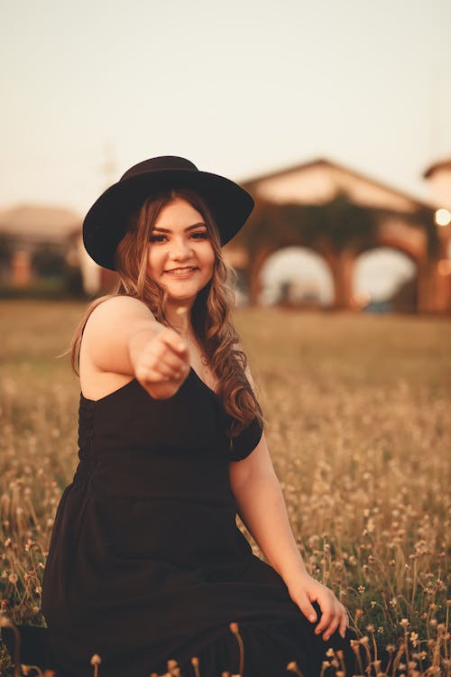 Woman in Black Dress and Black Hat Sitting on Grassfield