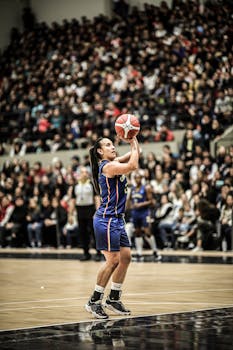Woman athlete taking a shot during a basketball game in an indoor gym.