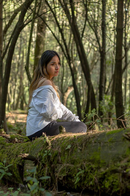 Woman in White Long Sleeve Shirt Sitting on a Mossy Wood Log