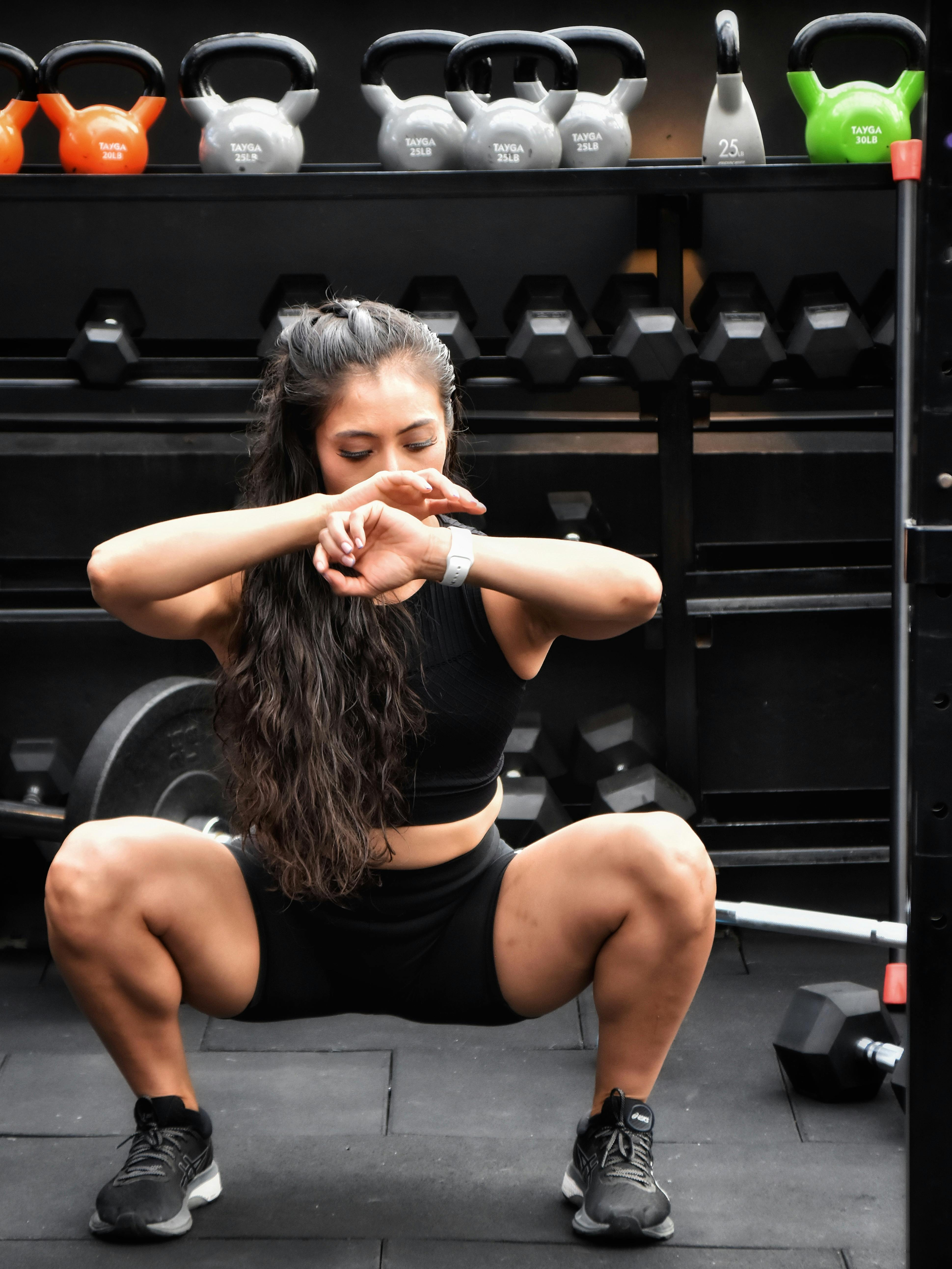 Woman performing a bodyweight squat with good form in a bright, airy home gym.