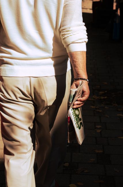 Man walks holding a newspaper on a sunlit street in Tirana, Albania.