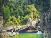 一对夫妇站在瀑布附近的岩石上，周围环绕着郁郁葱葱的茂密森林，风景优美