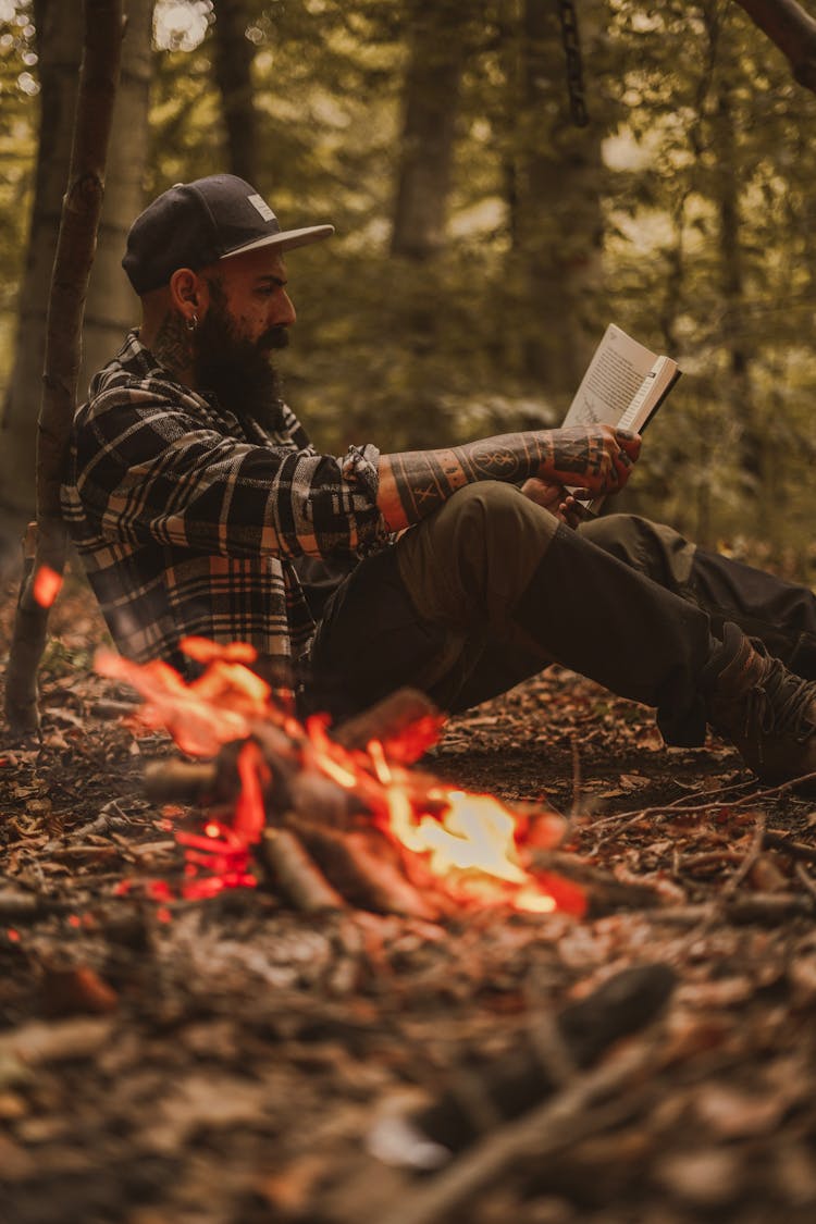 Man Sitting By The Fire In The Forest And Reading A Book 