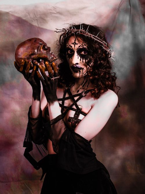 Free Eerie portrait of a woman in dark attire, holding a skull with gothic-themed face paint. Stock Photo
