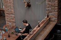 一名成年男性在乡村咖啡馆里使用笔记本电脑，旁边放着咖啡和木制装饰