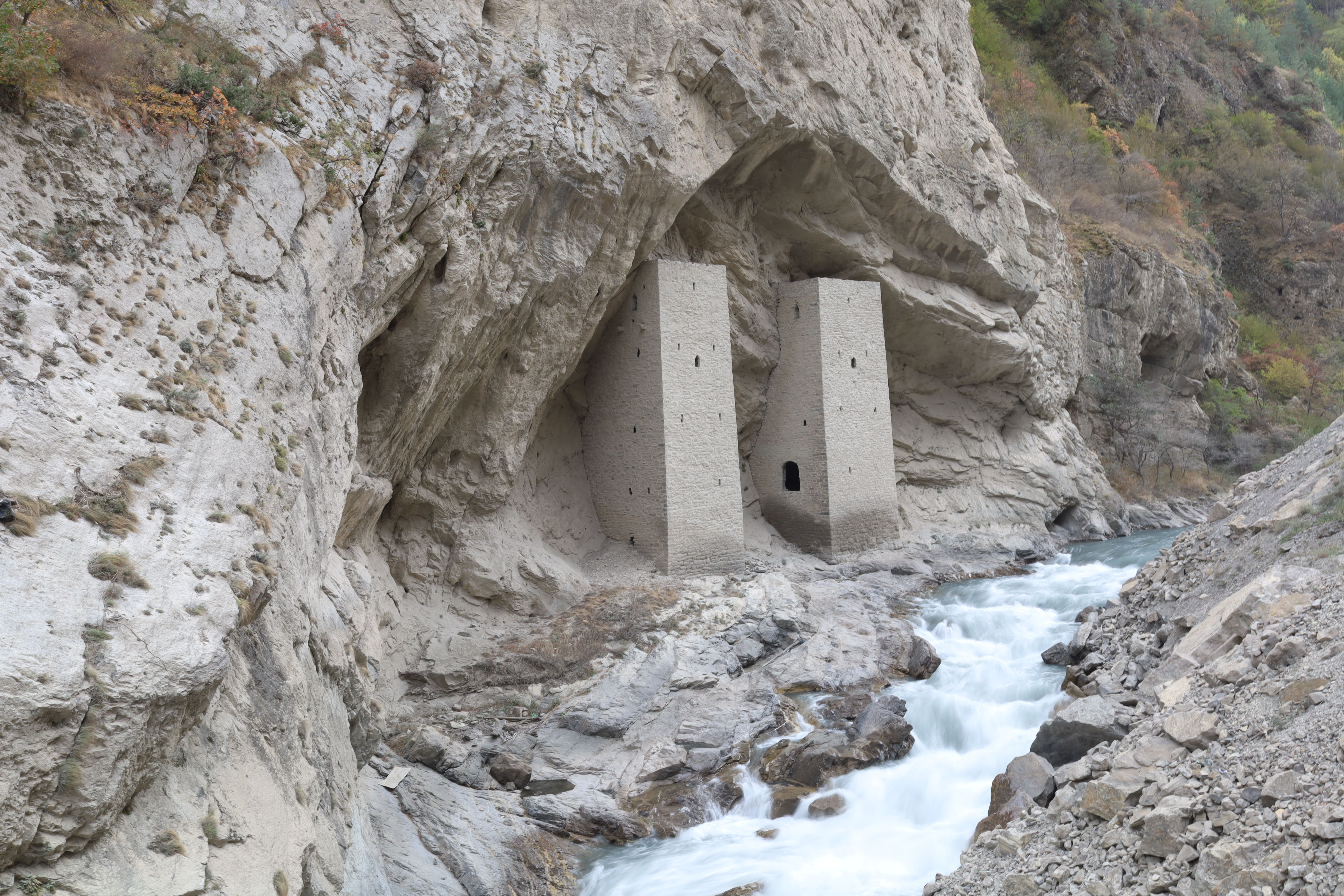 Ancient Ushkaloy Towers nestled in rugged Caucasus landscape with a flowing river.