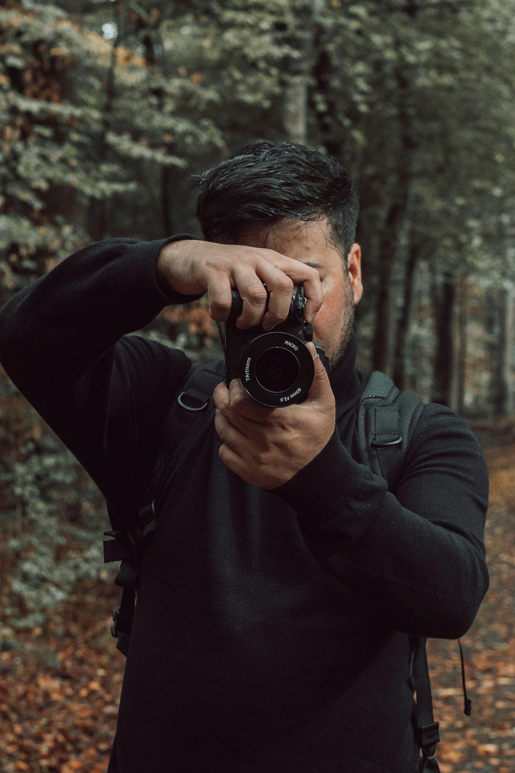 Man photographing autumn landscape in forest, wearing black sweater.
