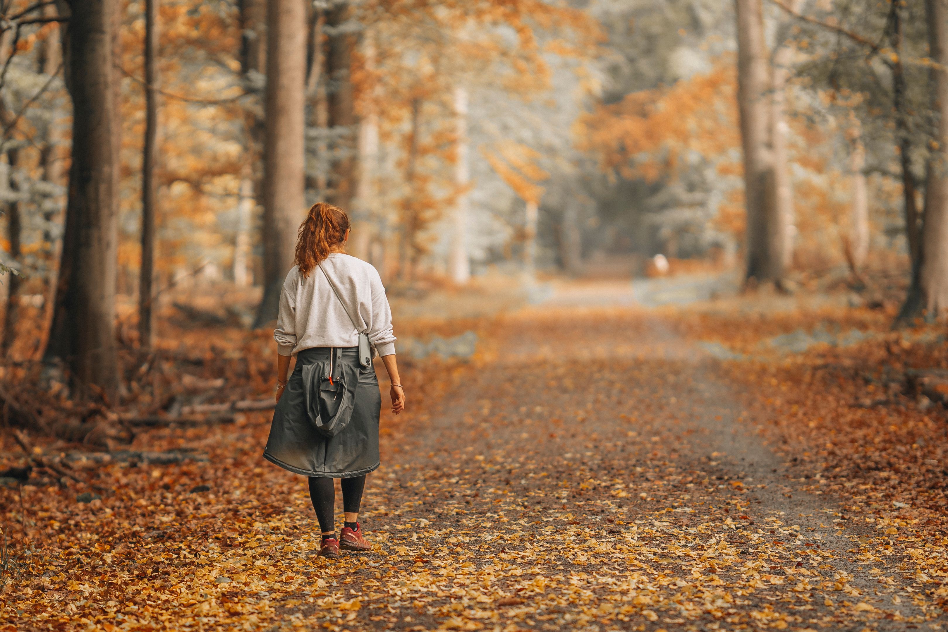 A woman strolls on a leaf-covered path through an enchanting autumn forest.